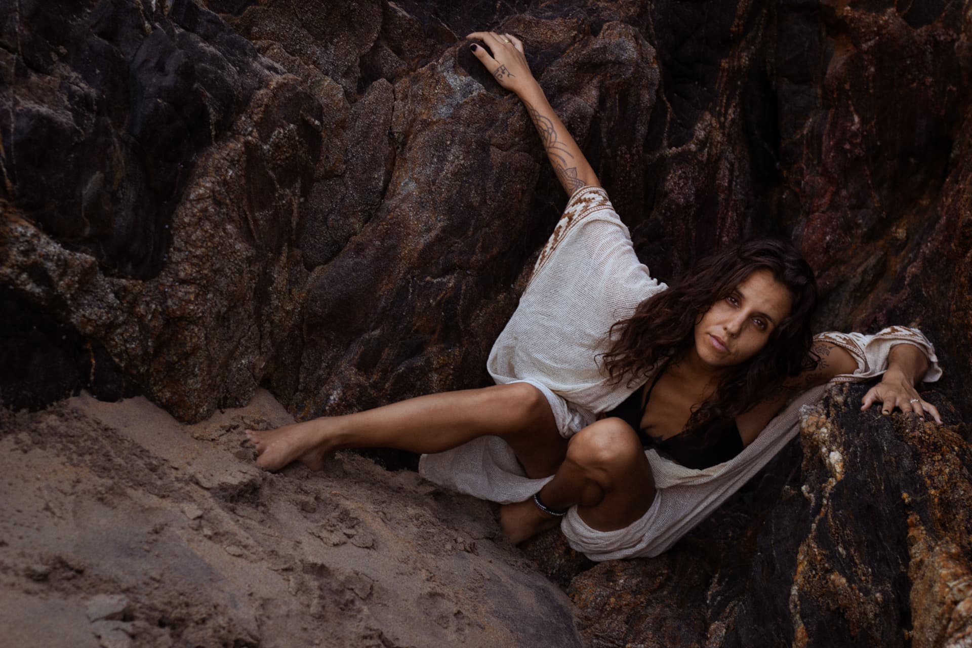 A woman resting among sunlit coastal rocks and sand